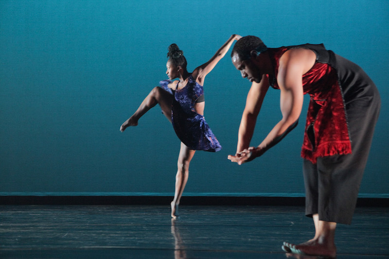 Coral Dolphin in the back ground, her left in an attitude position and Keon tholouis the foreground making a gesture with his hands toward the floor in Exotica. Photo: Ayodele Casel.